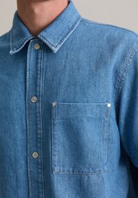 Lichtblauwe denimshirt met een klassieke kraag, voorflap met drukknoopjes en een borstzak met decoratieve klinknagels.