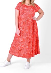 Krótka sukienka z krótkim rękawem, do kostek, w jasnym czerwonym kolorze z wzorem paisley, z marszczonym talią, noszona z białymi trampkami.