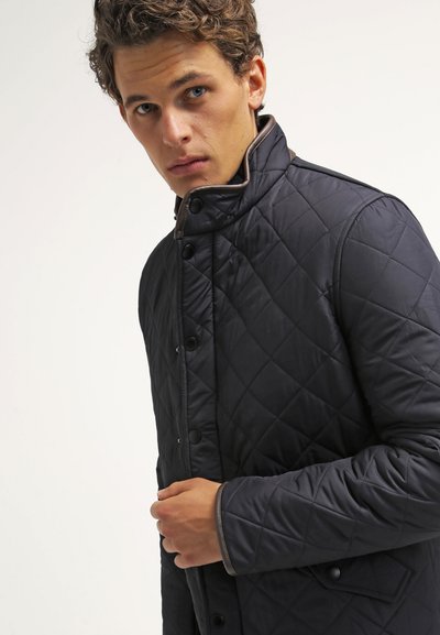 Veste matelassée bleu marine avec un col montant, ornée d'un motif en losange, de boutons sur le devant et d'accents marron sur le col et les poignets.