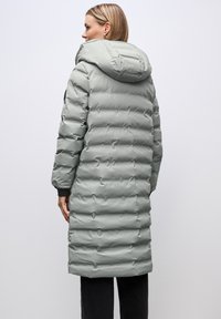 Puffjacka i ljusgrått med huva, med kuddad design, elastiska muddar och knälång längd. Slät, glänsande yta.