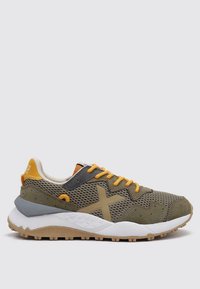 Zapatilla deportiva de malla verde y ante con cordones naranjas, acentos grises y una suela de goma blanca que presenta un patrón de agarre texturizado.