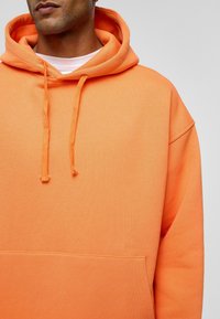 Oranje hoodie met een zachte textuur, voorzien van een kangoeroezak en trekkoorden, ontworpen met een relaxte pasvorm.
