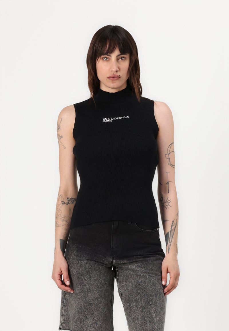 Juodas be rankovių golfo megztinis su balta siuvinėta "KARL LAGERFELD JEANS" logotipu kairėje pusėje, derinamas su tamsiai pilkomis džinsomis.