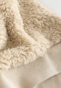 Beige textured fabric featuring a soft, fluffy, shearling-like surface paired with a smooth woven base, showcasing a layered design.