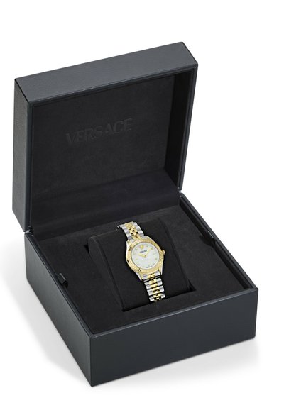 Reloj Versace en una caja negra, con una correa de plata y oro, un dial redondo blanco y un bisel dorado texturizado.