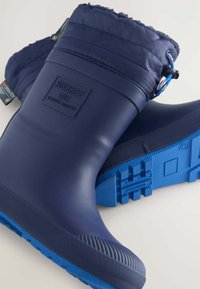 Bottes de pluie en caoutchouc imperméables de couleur marine avec un haut rembourré, une semelle bleu contrastée, une texture antidérapante et un logo sur le côté.
