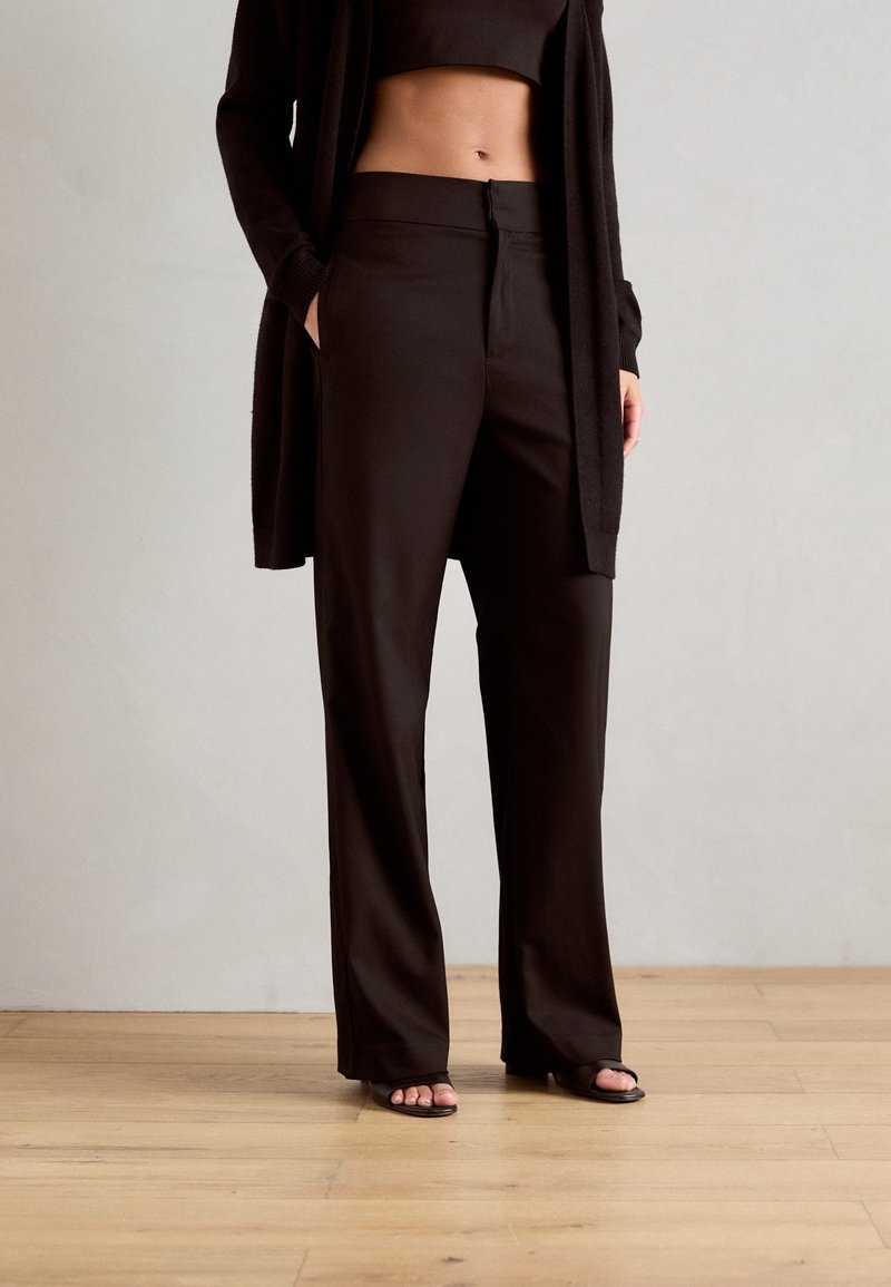 Pantalones negros de pierna ancha hechos de tela suave con un frente liso y bolsillos laterales, combinados con un top corto y un cárdigan. Diseño simple y moderno.