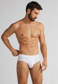 Vita bomullstrosor med en slät textur, elastisk midjeband och en frontficka design, figurnära stil, inga synliga mönster eller detaljer.