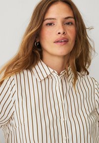 Striped button-up shirt in cream with brown vertical stripes. Features a collar and front buttons. Soft, lightweight fabric with a smooth texture.