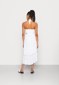Vestido branco de halter, corpete ajustado com detalhes recortados na cintura, saia fluida com barra franzida, sapatos planos usados.