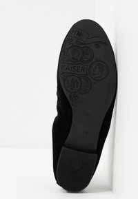 Sort ruskindssål med prægede mønstre, herunder et ansigt, teksten "KAISER" og andre dekorerende detaljer. Flad gummihæl for stabilitet.