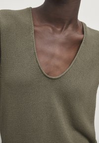 Olive green knitted top with a deep V-neck and wide shoulder design, featuring a textured fabric and seamless edges.