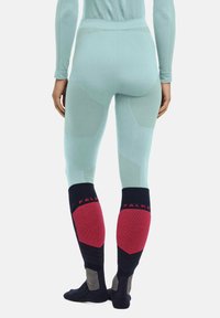 Wärmelégins in hellem Minzgrün mit strukturierten Akzenten; mit dunklen Socken, die rote und graue Patches in der Wadenhöhe aufweisen.