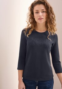 Dunkelblaues Sweatshirt mit Dreiviertelärmeln, das auf der Vorderseite ein strukturiertes Design mit "CREATE INSPIRE" aus Strasssteinen aufweist. Weicher Stoff.
