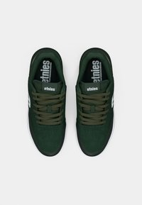 Πράσινα σουέτ αθλητικά παπούτσια με δέσιμο, που έχουν λευκό λογότυπο στο πλάι και υφή στην γλώσσα. Ραμμένο λάστιχο με στρογγυλή μύτη.