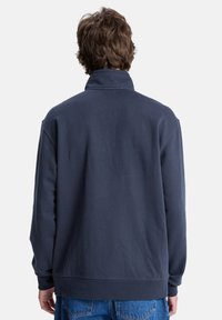 Dunkelblauer Sweatshirt mit hohem Kragen, langen Ärmeln und lockerer Passform. Glatte Textur und minimale Details auf der Rückseite.