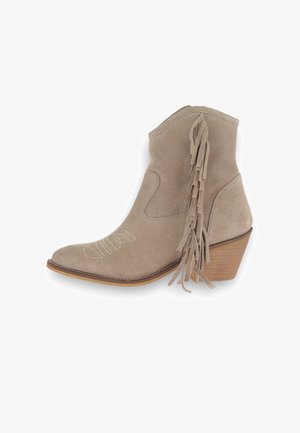 Botín de ante beige hasta el tobillo con punta afilada, detalles de flecos en el talón y tacón apilado. Presenta acentos bordados en el costado.