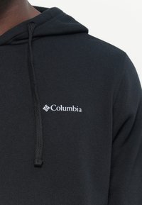 Felpa nera con cappuccio realizzata in tessuto morbido, dotata di una tasca frontale a marsupio, cappuccio regolabile con coulisse e un logo Columbia bianco sul petto.
