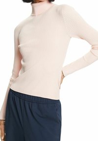 Suéter de cuello alto de color rosa claro con relieve, de mangas largas, diseño ajustado y textura suave. Combinado con pantalones oscuros y holgados.