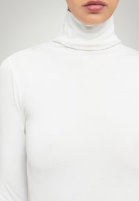 Vit polotröja i mjukt tyg, med en figurnära design och långa ärmar, samt en högkrage.