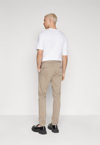 Beige chinos with a slim fit, paired with a plain white t-shirt. Black shoes and two back pockets, shown from the back. Smooth texture.