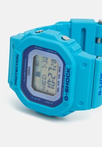 Orologio digitale blu con cinturino in gomma, quadrante quadrato e lunetta protettiva. Presenta indicatori di allerta, luce e resistenza all'acqua.