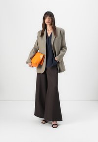 Sacou supradimensionat de măslină, bluză bleumarin, pantaloni maro cu picioare largi, poșetă portocalie și sandale negre. Tesături netede, forme structurale și culori îndrăznețe.