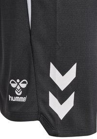 Črno teksturirano blago z belim logotipom Hummel na levi strani ter dvema belima navzdol usmerjenima chevronoma na desni strani oblačila.