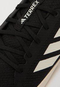 Svart idrottssko med nätövre del, utrustad med svarta snören, vit adidas tre-rands logotyp och strukturerad gummisula i off-white.