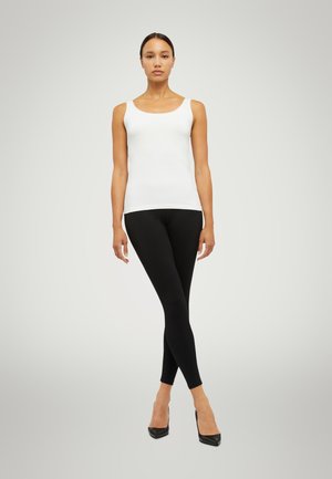 Top bianco senza maniche, leggings neri e tacchi alti neri. Il top ha un scollatura a barca ed è aderente; i leggings sono lisci e elasticizzati.