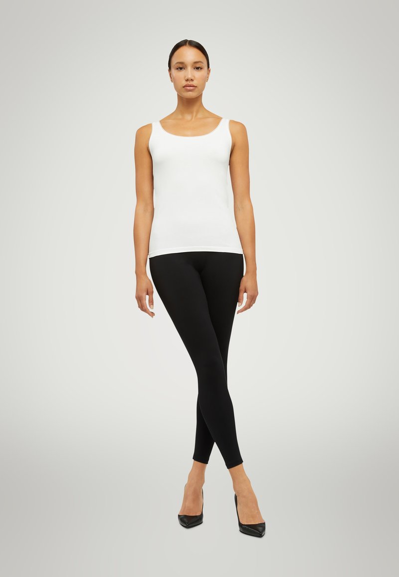 Vitt linne, svarta leggings och svarta högklackade skor. Linnet har en rundad urringning och sitter tajt; leggingsen är släta och töjbara.