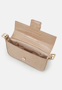 Handväska i ljusbeige med krokodilstruktur, prydd med ett guldknäpp, som har ett rymligt innerrum och en dragkedjeficka.