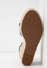 Semelle d'une sandale compensée taille 37 avec dessous en caoutchouc brun, plateforme en jute tissé et brides en tissu bleu, présentée sur fond blanc.