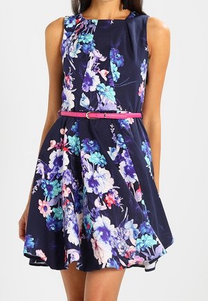 Ærmeløs navyblå kjole med flerfarvet blomsterprint, plisseret nederdel og slank pink bælte ved taljen.