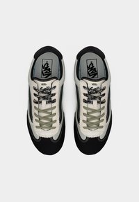 Paire de baskets Vans avec des panneaux noir, blanc et gris, des lacets contrastants, et le logo "Vans" sur la semelle intérieure, vue de dessus.