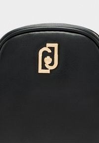Schwarzer Leder-Rucksack mit runder Oberseite, glatter Textur und einem auffälligen Logoakzent in Gold auf der Vorderseite.