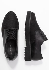 Chaussures noires à lacets avec un dessus tissé texturé, des accents en cuir lisse et une semelle en caoutchouc épaisse présentant des bords nervurés.