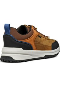 Zapatilla deportiva marrón y negra con materiales de ante y malla, que cuenta con una suela de goma texturizada, diseño de cordones y un acento azul en el talón.