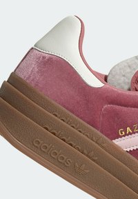 Tenisky Gazelle v jemné růžové velurové úpravě s bílými koženými akcenty, s texturovanou hnědou gumovou podrážkou a zlatými detaily s logem.