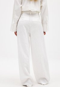 Baltas brīvi pieguļošs lina bikses ar augstu jostasvietu, ar aizmugures kabatām un teksturētu apdari. Apvienotas ar līdzīgas krāsas īsu topu.