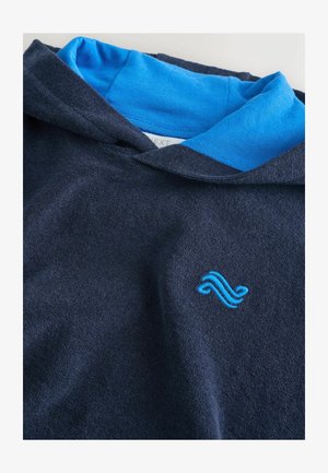 Tmavomodrá mikina s kapucňou s bledomodrou vnútornou podšívkou a malým modrým vyšitým logom vlny na prednej strane. Mäkká, štruktúrovaná látka.