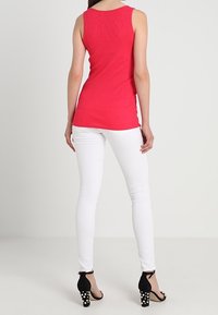 Rød ribbet tanktop, hvide skinny jeans og sorte højhælede sko med hvide polka dots. Simpelt design og tætsiddende silhuet.