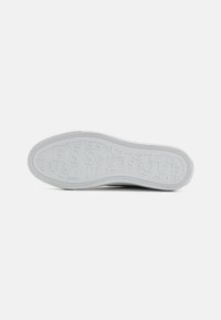 Vit sneakersula med ett texturerat mönster där varumärket "GUESS" är präglat. Rundade kanter och en tydlig mönstring är synliga.