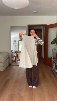 Jupe blanche en tissu lisse, évasée en bas, tenue par une personne portant une chemise rayée. Cadre intérieur chaleureux avec des accents en bois.