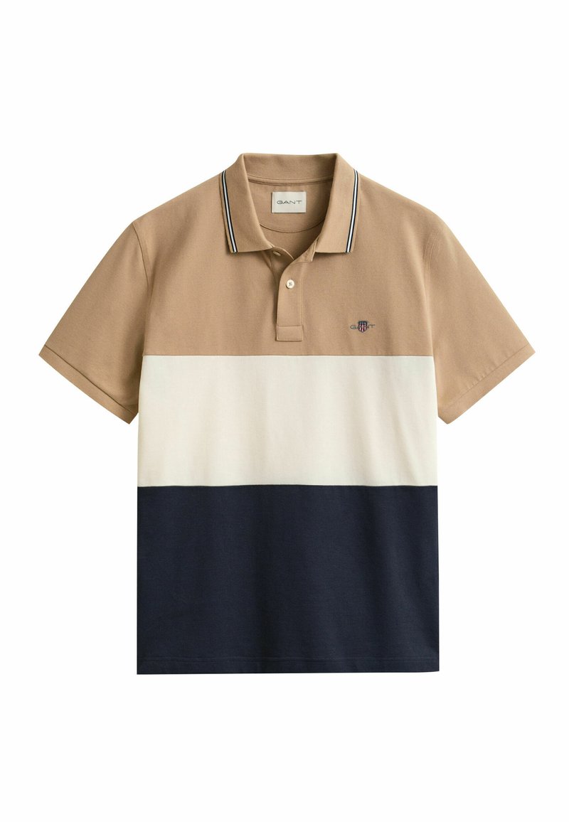 Polo à manches courtes avec haut beige, milieu blanc, bas bleu marine, patte à deux boutons et petit logo brodé sur la poitrine.