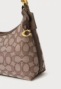 Ruskea ja beige käsilaukku, jossa on kuviollinen kangas, sileäpintainen pinta, kullanvärinen yksityiskohta ja ketjuolkaiminen kantohihna.