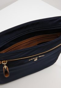 Borsa in tessuto blu navy con una cerniera dorata, dettagli interni marroni e scomparti multipli per l'organizzazione. Texture liscia e design elegante.