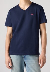 Námořnická modrá bavlněná tričko s krátkým rukávem a výstřihem do V, s malým červeným logem Levi's na hrudi. Jednoduchý, klasický design.