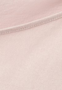 Détail de couture sur un tissu rose clair montrant une texture tricotée fine et une couture serrée et régulière le long d'un bord courbe.