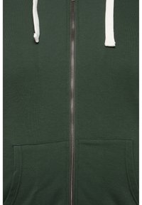 Sudadera verde con cremallera y cordones blancos, con bolsillos en la parte frontal, hecha de una tela suave con una textura lisa y una cremallera metálica.